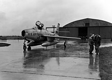 Photographie en noir et blanc d'un Republic F-84 Thunderjet devant un hangar sur une base militaire.