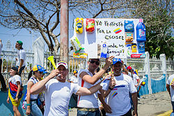 A protester during the 2014 Venezuelan protests holding a sign saying, "Yo protesto por la escasez. Donde los consigo?" (I protest for the scarcity. Where can I get these?). Marcha hacia el Palacio de Justicia de Maracaibo - Venezuela 16.jpg