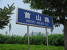 A Shou Shan Road (首山路) sign featuring the façade of Shoushan (首山) beyond the overgrowth in the background in Xingcheng.