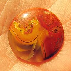 A round cabochon of Tennessee paint rock showing clear holding agate, white banding and a red mossy formation.