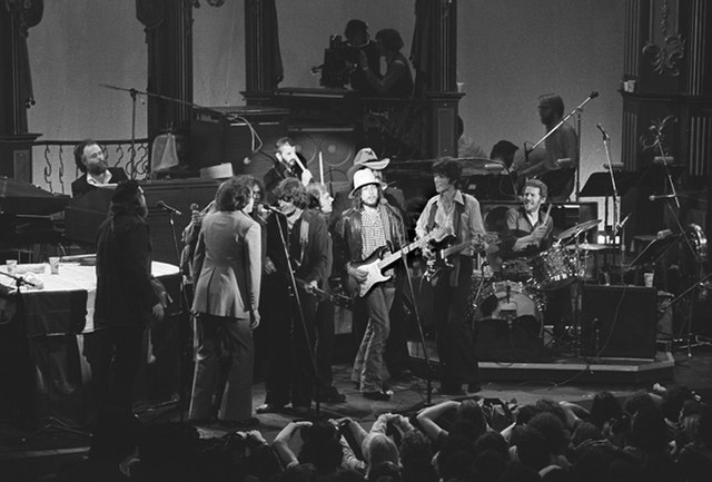 Photograph of The Last Waltz. The Band with Bob Dylan and other guests performing I Shall Be Released. seated behind instruments: Garth Hudson (organ)