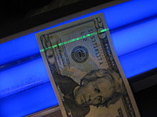 Fluorescent security strip in a US twenty dollar bill under UV light US $20 under blacklight.jpg