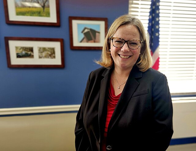 Photograph of Undersecretary Moffitt in her office in front of American flag and pictures of her family's organic walnut farm