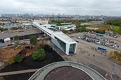 Het station met loopbrug tussen de twee ronde toegangsgebouwen van de metro, gezien uit het zuiden