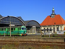 Das Empfangsgebäude von Süden und die Bahnhofshallen mit den verglasten Treppenaufgängen und ausfahrender Diesellokomotive SU46 007 der PKP