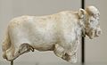 A carved, white statue of a bull missing its legs and with a head showing details of ears, mouth, nose, and eyes