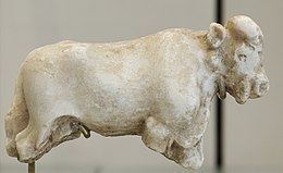 A carved, white statue of a bull missing its legs and with a head showing details of ears, mouth, nose, and eyes