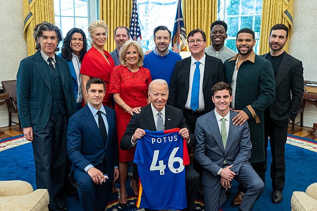 President Joe Biden, holding an AFC Richmond jersey, and First Lady Jill Biden greet the cast of Ted Lasso in the Oval Office on March 20, 2023.