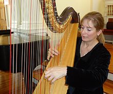 Harpist Elaine Christy plays with both hands approaching the strings from either side of the harp; foot pedals (not shown) can change the pitch of specific strings by a half step. Harpist Elaine Christy at Unitarian Church 2.jpg