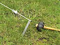 A light gauge pressed metal tent peg, with rope and mallet.