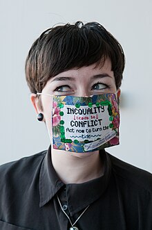 A woman wearing a craftivist facemask. Laura trying on craftivism mask.jpg