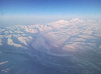 Luftaufnahme des Denali und der schneebedeckten Alaska Range mit einem Gletscher, der zu einem Fluss führt