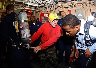 Aviation Ordnanceman explains how to use the Self Contained Breathing Apparatus (SCBA). US Navy 060608-N-5917H-001 Aviation Ordnanceman 1st Class Jacques Beaver explains how to use the Self Contained Breathing Apparatus (SCBA) to Culinary Specialist Seaman Jonathan Lewis.jpg