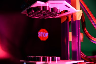 An acoustophoretic volumetric display where a small expanded polystyrene particle is rapidly moved with light projected onto it to produce the image of a 'stop sign'. This is a composite image taken over 20 seconds. Acoustophoretic Volumetric Display.jpg