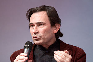 Photograph of a middle-aged man speaking into a microphone.