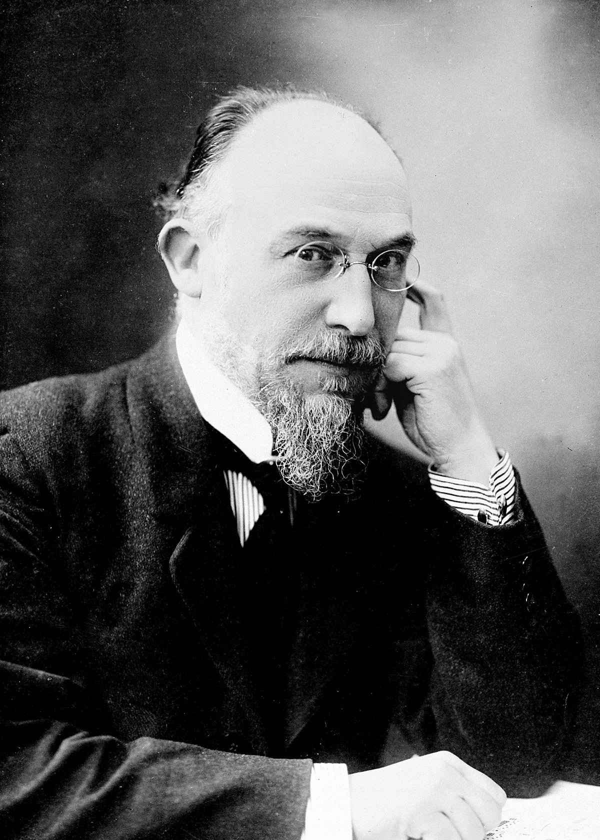 Erik Satie with glasses looking stern and fanciful.