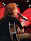 La vue latérale d'une femme les yeux fermés, chantant dans un micro et jouant de la guitare noire.