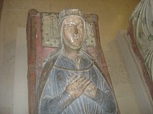 Une photographie d'une tombe médiévale avec une sculpture d'Isabelle sur le dessus.  Elle est allongée, les mains jointes, vêtue d'une robe bleue.