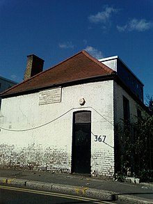 Фотография простого белого кирпичного дома с красной крышей и черной дверью.