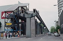 A city street with the elevated monorail guideway, cut short to display the hollow steel tracks. A temporary stairway and elevator structure had been erected to the side to provide access.