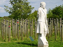 White statue of a man with a blindfold, in front of wooden posts.