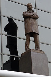 A bronze statue of a man wearing a coat with his arms folded.