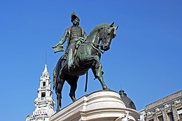 Photograph of a bronze statue with a man on horseback wearing a bicorn hat and military dress and who holds forth a scrolled sheaf of paper