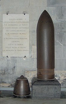 15-inch British naval APCBC shell with its armour-piercing cap on the floor to the left; the ballistic cap is absent. Fired 1941 but did not detonate. Genoa Cathedral Unexploded shell in the cathedral in Genoa (Italy) (cropped).jpg