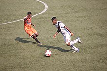 Vasco SC player (in white) in action during a Goa Pro League match against FC Goa Reserves in April 2021 Vasco SC Goa player in action during a Goa Pro League match against FC Goa Reserves in Duler Stadium, Mapusa, April 13, 2021.jpg