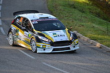 Coche blanco, amarillo y negro, tres cuartos, en una curva.