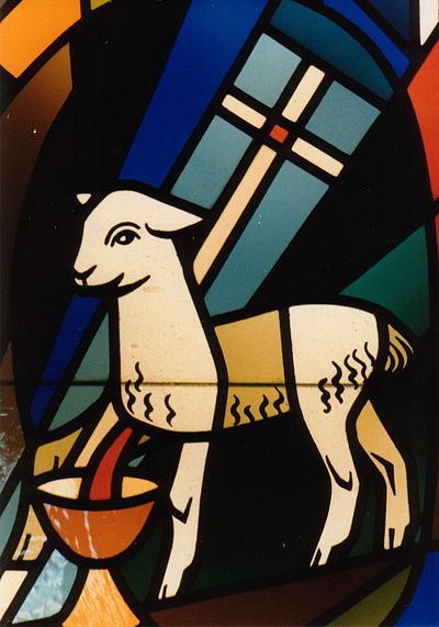 The Lamb of God with a vexillum and chalice in stained glass, a symbol of Christ as the perfect sacrifice.