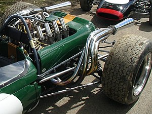 Primer plano de la parte trasera de un coche de carreras verde, mostrando el motor, los escapes, la suspensión trasera y las ruedas traseras