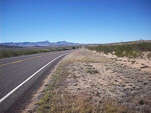 Image of FM 3078 passing through desert shrub land with the Davis Mountains looming in the distance.