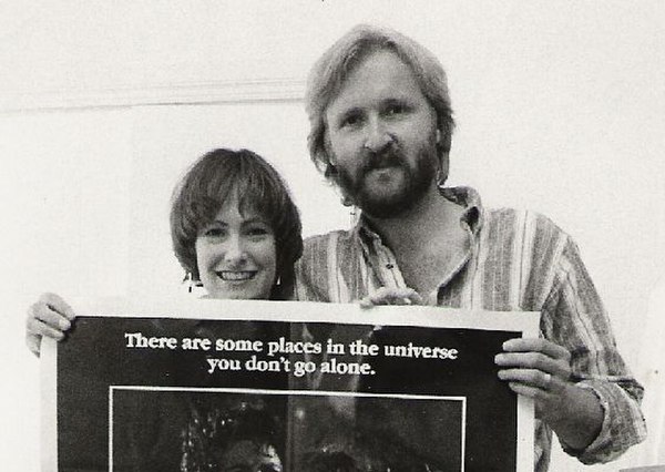 Cameron and Hurd holding a theatrical poster for Aliens in 1986