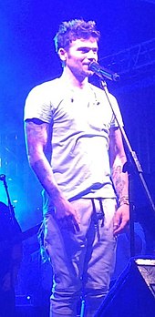 Shot of Pedro Capó smiling in front of a microphone, wearing a white shirt.