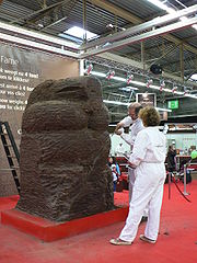 Dans une vaste salle d'exposition trône une sculpture chocolatière géante ; se tiennent à côté les deux sculpteurs en action.