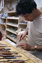 a man carving a strip of wood with carving tools lined up in front of his workstation
