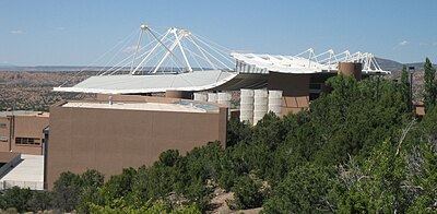 Santa Fe Opera's Crosby Theatre viewed from the south showing the unusual roof line and how it is supported. The white, sail-like wind baffles (centre, middle distance) are designed to limit rain from entering the theatre.