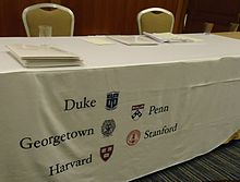 Elite and other universities send admissions officers to high schools and college fairs to encourage high school students to apply. While the chance of admission to highly selective colleges is typically under 10%, increased numbers of applications helps maintain and improve colleges' rankings. Table and banner at college admissions presentation.jpg