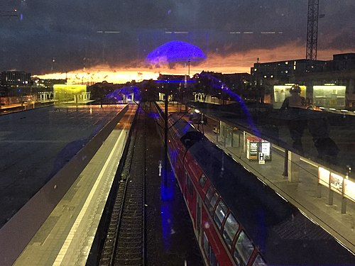 View through glass panes of a station concourse at tracks, train, sunset and reflections