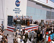 Dignitaries on an outdoor stage in front of a building with NASA Manned Spacecraft Center on the side