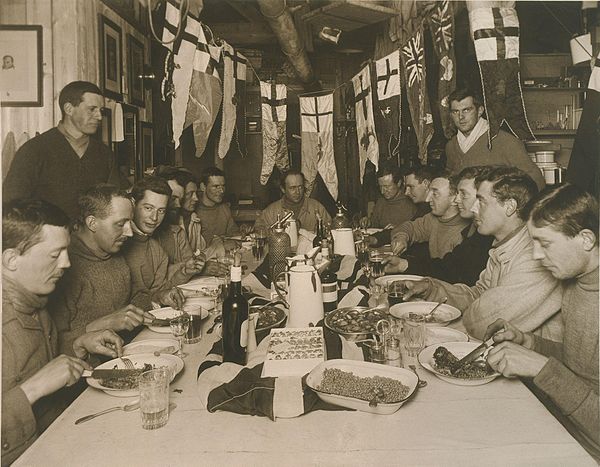 Photo of 15 men feasting at a table with Scott at center