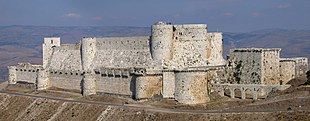 Eine steinerne Burg mit zwei hohen Ringmauern, eine in der anderen.  Sie sind mit Zinnen versehen und mit vorspringenden Türmen besetzt, sowohl rechteckig als auch abgerundet.  Das Schloss liegt auf einer Landzunge hoch über der umliegenden Landschaft.