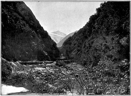 A river in between two mountains. There are more mountains in the distant fog.