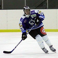 Photographie d'une joueuse de hockey avec une tenue renforcée et une crosse à la main.