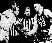 Jerry Harkness and Joe Dan Gold shake hands in front of two referees.