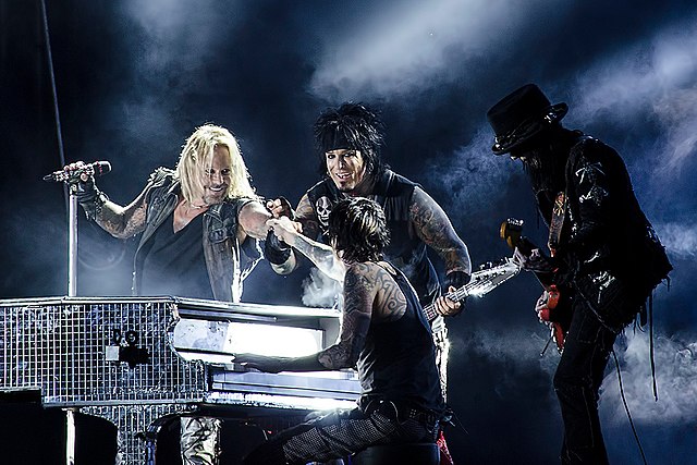 Mötley Crüe performing live in 2012, from left to right: Vince Neil, Nikki Sixx (background), Tommy Lee (foreground), Mick Mars