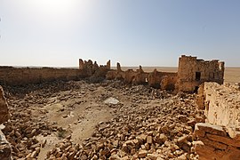 Cour couverte de moellons entourée de murs en ruine.