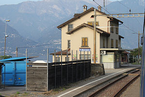 Dreistöckiges Gebäude mit Satteldach neben zweigleisiger Eisenbahnlinie