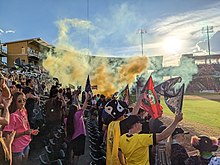 Supporters with flags revel in the celebratory smoke following a goal by New Mexico United in the 1st minute of their match versus Pittsburgh Riverhounds SC on 16 July 2022 Supporters with flags revel in the celebratory smoke following a goal by New Mexico United in the 1st minute of their match versus Pittsburgh Riverhounds SC on 16 July 2022.jpg